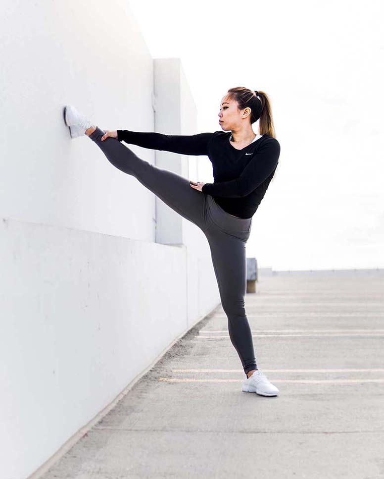 A woman does leg stretches against a wall.