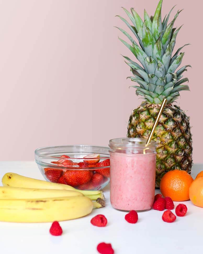 An array of fruit surround a smoothie.