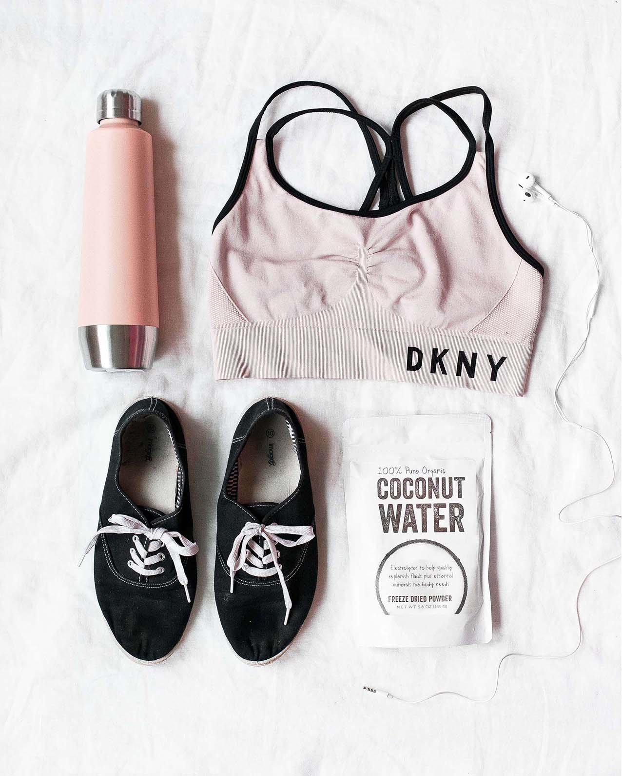 A water bottle, sports bra, sneakers, and coconut water laid out on a white cloth.