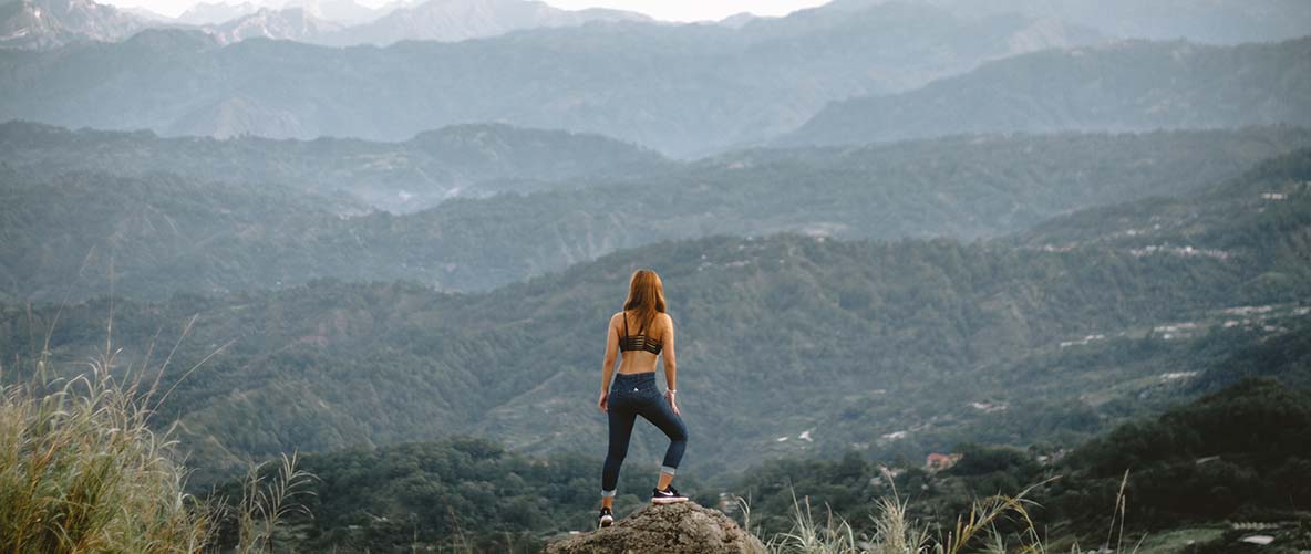 A woman in workout clothes looks out over a mountain.